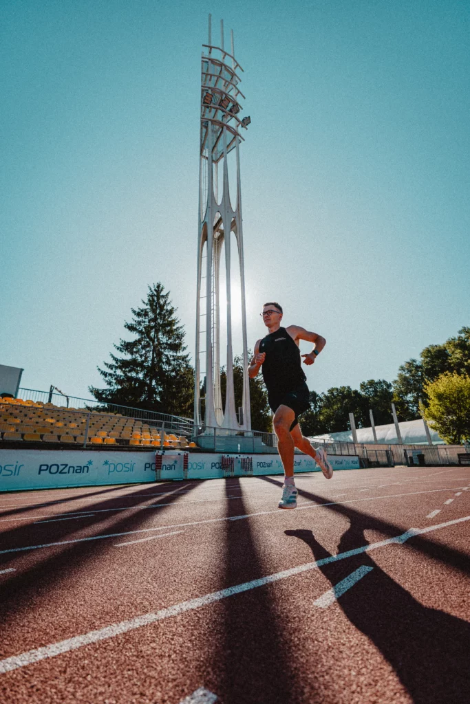 Piotr Tomczyk, trener biegania, biegnie na bieżni w blasku słońca.