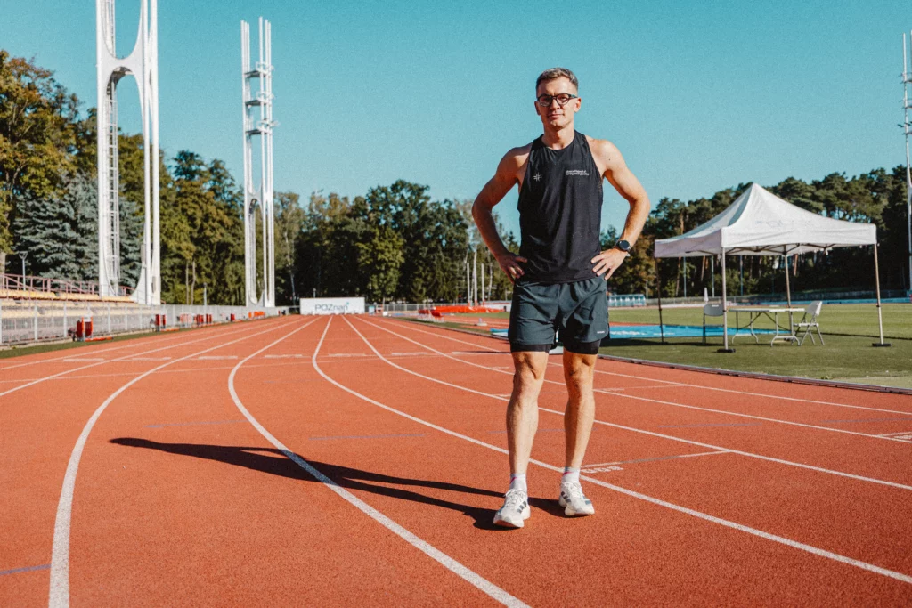 Piotr Tomczyk, trener biegania, stoi na bieżni na stadionie lekkoatletycznym w Poznaniu.