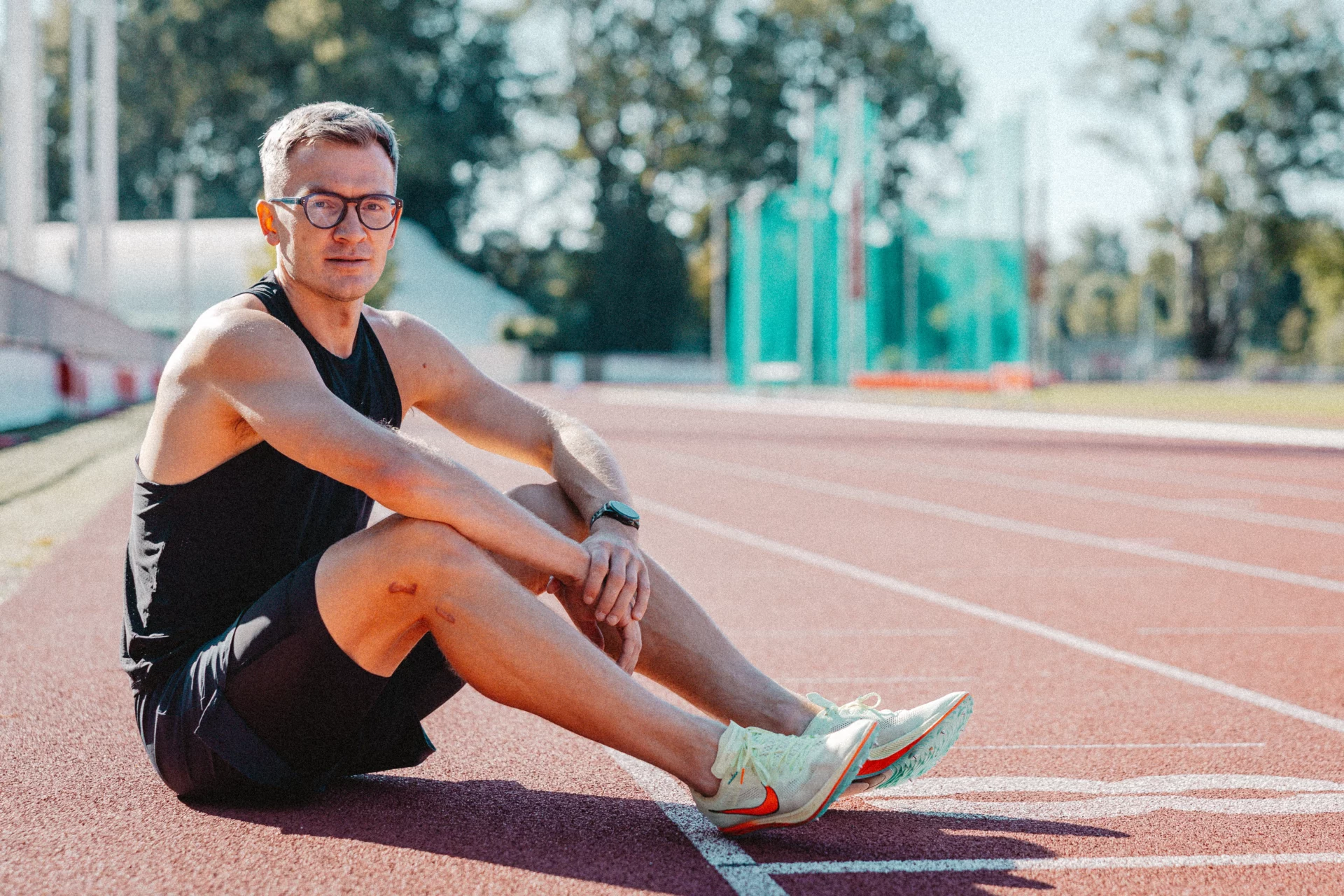 Piotr Tomczyk trener biegania siedzi na tartanie na stadionie lekkoatletycznym.